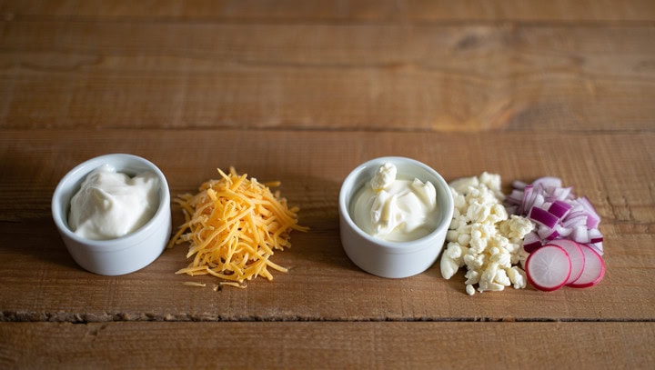 Queso cottage, queso rallado, requesón y cebolla morada, radicionales ingredientes en dietas para pérdida de peso y alimentación saludable, sobre una mesa de madera.