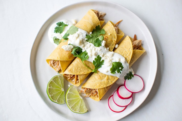 Sabrosos tacos de pollo desmenuzado con salsa, cilantro y rodajas de limón y rábano en plato blanco.