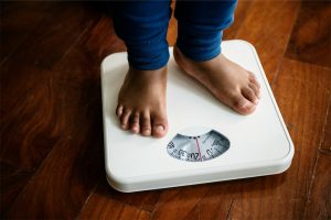 Niño de pie en balanza digital para medir peso infantil en casa.