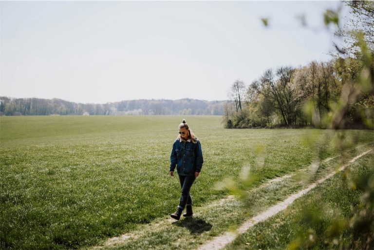 Woman walking on a grassy field in spring, enjoying outdoor leisure, scenic nature landscape, sunny weather, casual nature walk, fresh air, tranquil environment, serene rural setting.