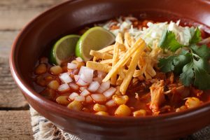 Arroz con verduras y pollo en un bol de barro, decorado con cilantro, cebolla, limón y totopos crujientes.