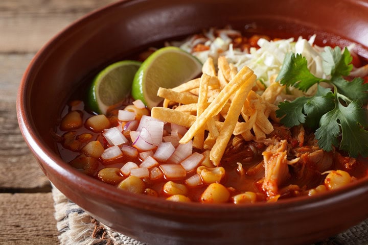 Arroz con verduras y pollo en un bol de barro, decorado con cilantro, cebolla, limón y totopos crujientes.