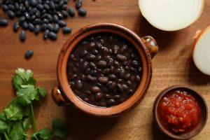 Pote de frijoles negros cocidos y sazonados con cilantro, cebolla y salsa roja en un entorno rústico.
