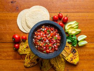 Refresco de agua fresca de tomate con jarra y variedad de ingredientes frescos sobre mesa de madera.